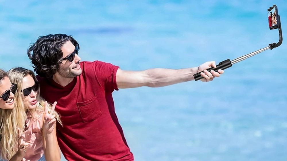 A man taking a pic of himself and two friends at the beach with Yoozon selfie stick. 